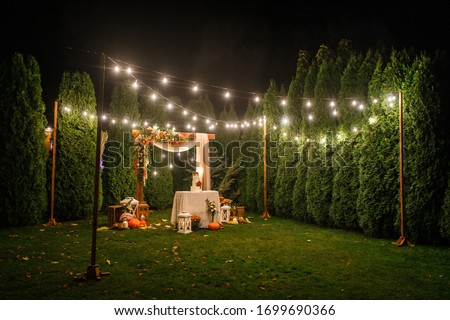 night wedding ceremony, the arch is decorated with flowers, candles and garlands of light bulbs and there is a wedding cake on the table Royalty-Free Stock Photo #1699690366
