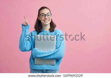 Smart looking girl student on pink colorful background holding her finger up to signal that she have an good idea while holding her computer