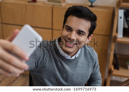 Selective focus of businessman smiling and taking selfie in office