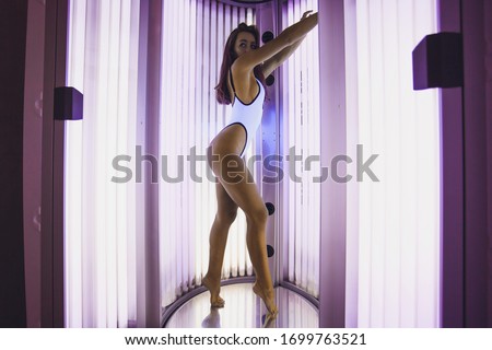 Solarium. Beautiful young girl in a bikini sunbathing in a vertical sunbed.