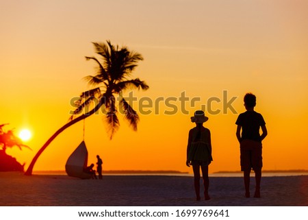 Silhouettes of two kids at tropical beach during sunset