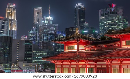 The Buddha Tooth Relic Temple comes alive at night view in Singapore Chinatown, with the city skyline in the background. The temple is brightly lit with skyscrapers and towers