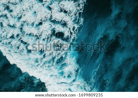 Aerial view of the raging blue ocean with textured waves and trouble foam during a storm