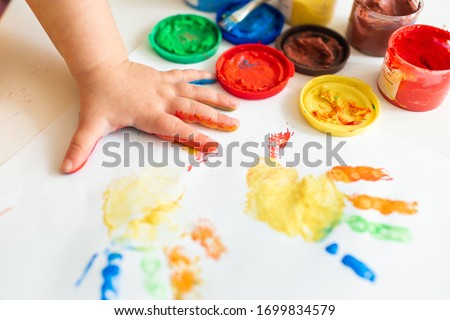 Close up of colored hand print on white background. Ideas for drawing with finger paints. Finger painting for kids. Little girl painting by finger hand paint color. Children development concept. Royalty-Free Stock Photo #1699834579