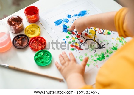 A child draws leafs on a tree. Ideas for drawing with finger paints. Finger painting for kids on white background. Little girl painting by finger hand paint color. Children development concept.  Royalty-Free Stock Photo #1699834597
