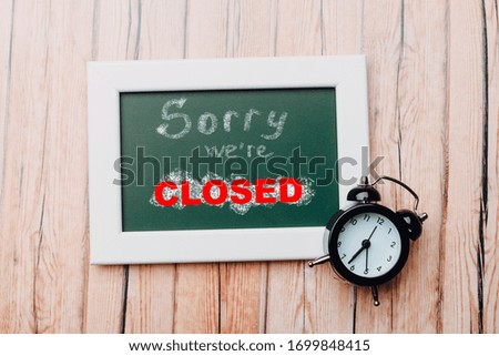 Sign "Sorry, we are closed" on a chalk board with English inscriptions on a wooden background. Closed business or store concept.