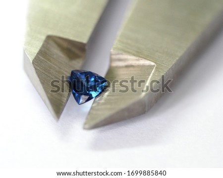 Isolated gemstone green blue red yellow held by jewelry tool tweezers on grey background with selective focus