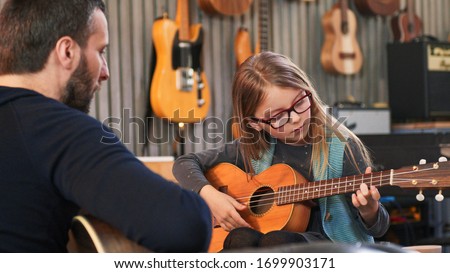 Dad teaching guitar and ukulele to his daughter.Little girl learning guitar at home.Close up.Ukulele class at home. Child learning guitar from her father Royalty-Free Stock Photo #1699903171
