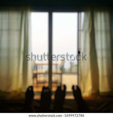 A picture of two people lying on the bed who could only see their feet lying outside the window, blurred background.