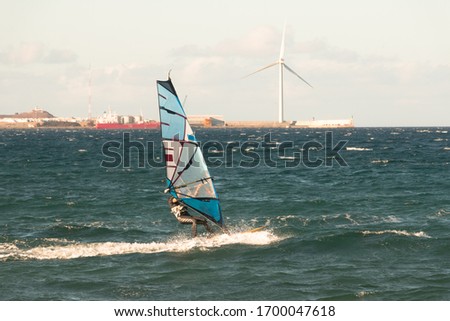 A surfer is racing with the wind and a wind turbine in the background. Sport concept