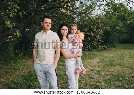 Portrait of a happy family in nature. A guy, a girl and a little daughter are hugging, standing in tracksuits in a green flowered garden. Photography, concept.