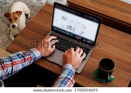 Cropped shot of unrcognizable man sitting on the couch, using laptop, browsing the web, drinking hot beverage. Working from home during self isolation period concept. Close up, copy space, background.