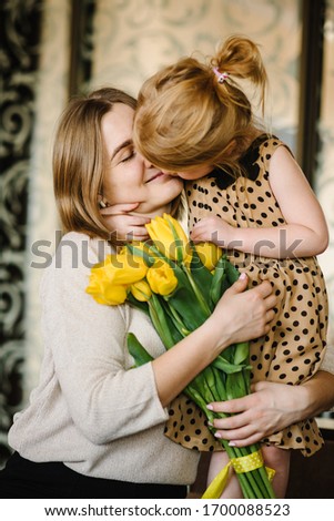 Happy mother's day. Daughter congratulates mom and gives her a bouquet of flowers tulips at home. Mom and child girl smiling, hugging and kissing. Family holiday and together.