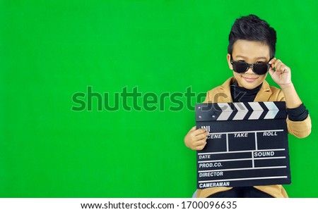 The boy held the slate film board and put his hand on the sunglasses. In order to take picture that look good and cool He has a mark of happiness and confidence in himself. He's very handsome and neat