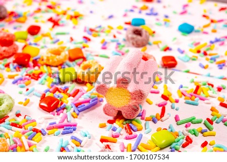 Colourful  sugar sprinkles, chiclets and marshmallow on light pink wood background.