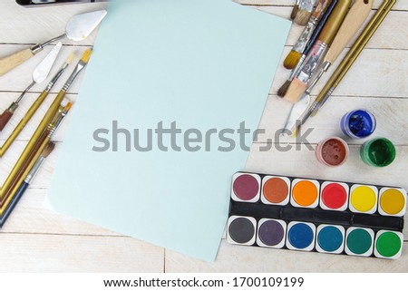 Set of artist accessories collection. Canvas, tube of oil paint, art brushes, palette knife and blue paper lying on the wood table. Artist workshop background.