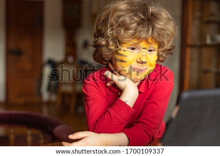 Little boy is watching TV. A child with a painted face is watching cartoons.