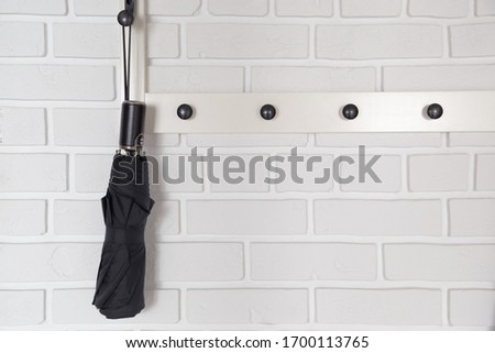 Black short umbrella hanging on hanger in white hallway interrior.