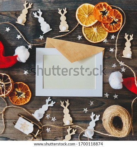 Christmas frame on wooden table with dry citruses, white and wooden toys, snowflakes, red christmas hats and bright silver stars. 