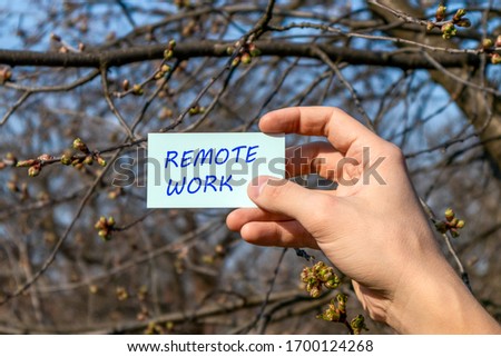 Remote work text on card holding in hand. Sunny nature, spring day outdoors, blue sky background. Free travel lifestyle