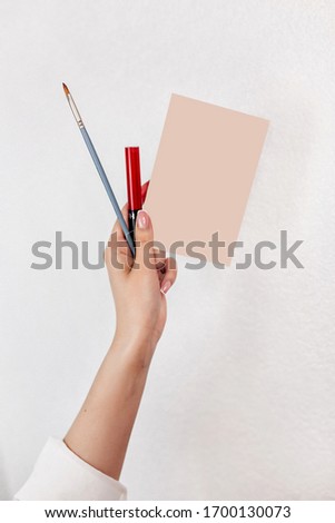 Female hand with business card of makeup artist and lipsticks and bruche on white background