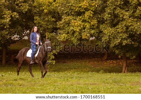 Young brunette woman with long hair posing with a brown red horse in a forest in a sunny meadow