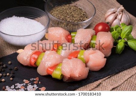 Chicken kebabs with tomatoes and spices on a black plate.