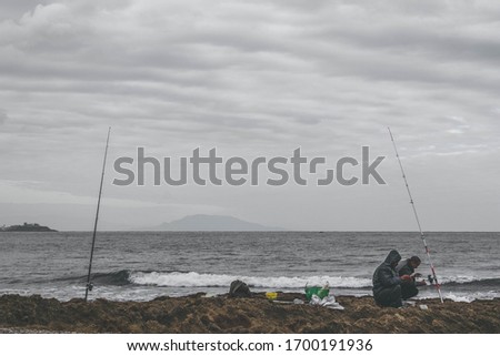 Fishers by the mediterranean sea at a rocky beach, on a cloudy day