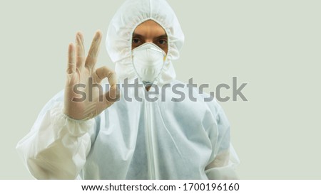 Doctor with mask and bioprotective suit with arm extended forward and his right hand making an OK sign on white background