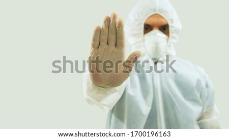 Doctor with mask and bioprotective suit with arm extended forward and his right hand open making a stop sign on white background