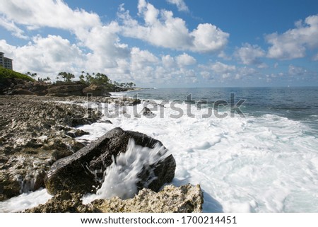 Tidal waves crash onto to shoreline rocks with puffy clouds overhead