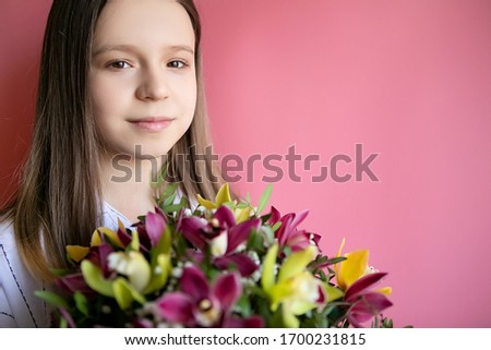 Teenager girl with a bouquet of colorful flowers on a pink background, place for text. Mother's Day Concept. Happy International Women's Day.
