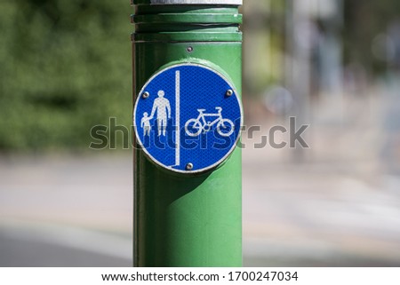 Road sign, pedestrian and bicyclist road sign pedestrian and bicyclist, in a green column. Circular blue traffic sign. Single object, white silhouette of a man holding a baby, and a bicycle