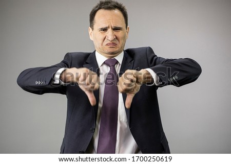 Disgusted middle aged businessman in formal clothes, tie showing dislake signs on isolated gray background with copy space. Portrait of displeased man, economy problems, taxes, small business concept