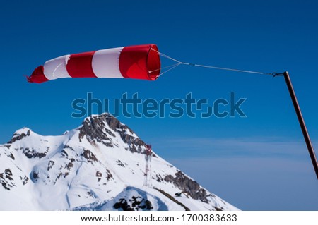 the red and white wind indicator is strongly developed against the background of the blue sky in the mountains Royalty-Free Stock Photo #1700383633