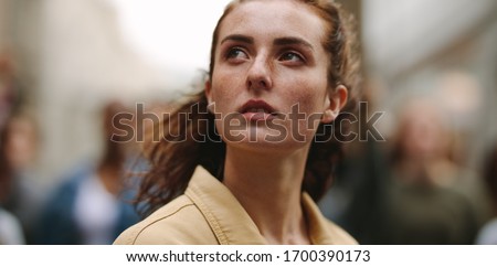 Close-up of woman activist looking away with group of protestors in background. Female activist demonstrating in the city. Royalty-Free Stock Photo #1700390173