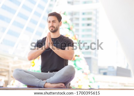 Iranian men wearing exercise clothes He was sitting cross-legged and sitting in the open air, with the background of a tall outdoor building. In the concept of yoga exercise for good health