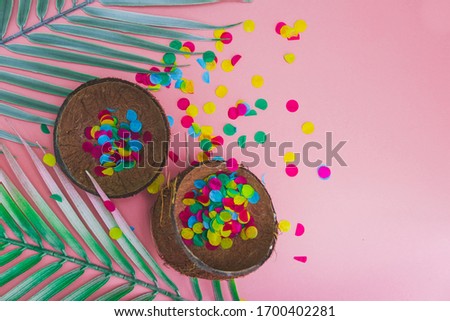 Coconut shells with confetti and palm leaves on pink background. Hot summer vacation concept. Tropical style. Flat lay.