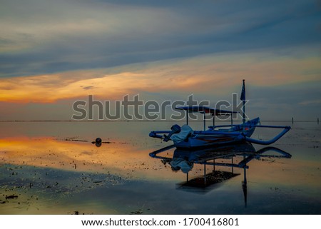 Seascape. Fisherman boat. Sunrise landscape. Traditional Balinese boat jukung. Fishing boat at the beach during sunrise. Water reflection. Slow shutter speed. Soft focus. Sanur beach, Bali, Indonesia.