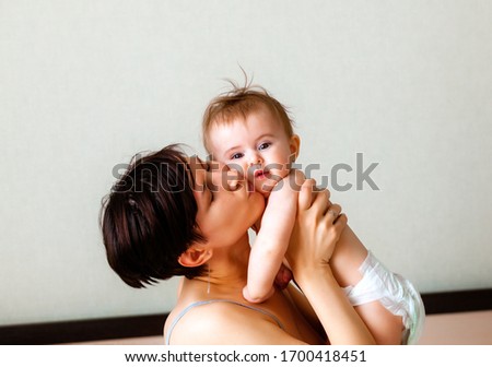 Happy cheerful family. Mom plays with her baby on the bed. Mom and baby kiss, laugh and hug.