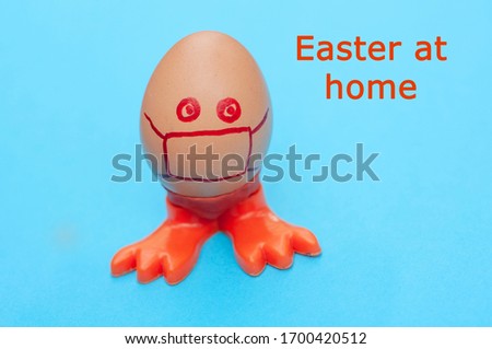 Egg with painted cartoon face in a medical mask on a blue background. Concept - stop coronavirus, corvid-19,stay at home. Easter at home lettering.