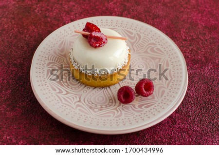 Contemporary coconut mini mousse tart decorated with fresh raspberries on white plate on red background