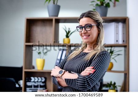 Attractive blonde woman with eyeglasses standing in office in front of office shelves