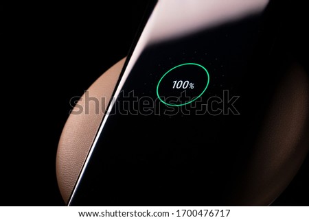 Smartphone Screen over Wireless Charger Showing a Fully Charged Battery. Phone Sitting in Charger Pad With Copy Space Royalty-Free Stock Photo #1700476717