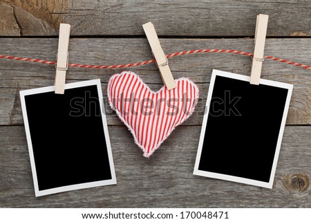 Two blank instant photos and red heart hanging. On wooden background