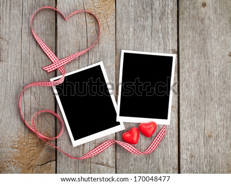 Two photo frames and small red candy heart on wooden background