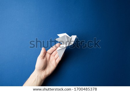 Origami pigeon  in human hands on a blue isolated background. World Peace Day concept. Close up studio photo.