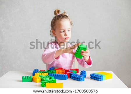 little girl is playing with a multi-colored plastic constructor, sitting at a white table