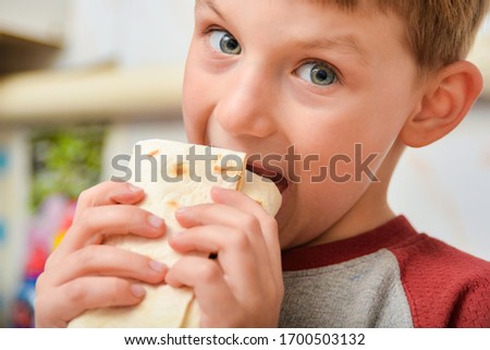 The boy holds shawarma in his hands, the child bites off meat wrapped in pita bread