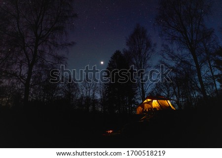 A campsite with a car with a roof top tent that shines and the planet Venus that shines brightly in the night sky among the stars